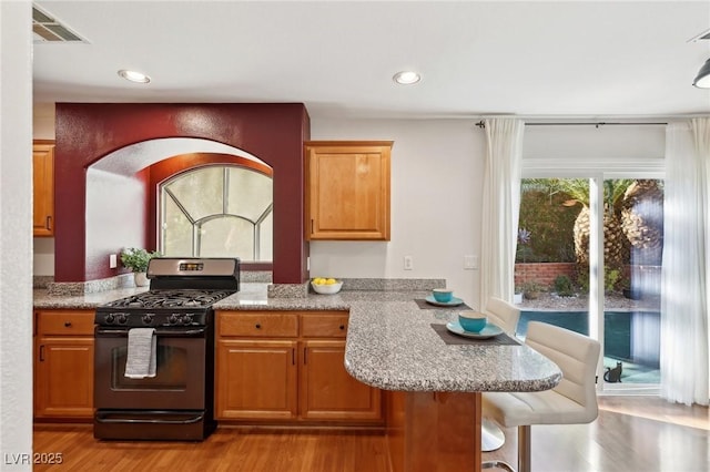 kitchen with black gas range, a kitchen breakfast bar, light stone countertops, kitchen peninsula, and light hardwood / wood-style flooring