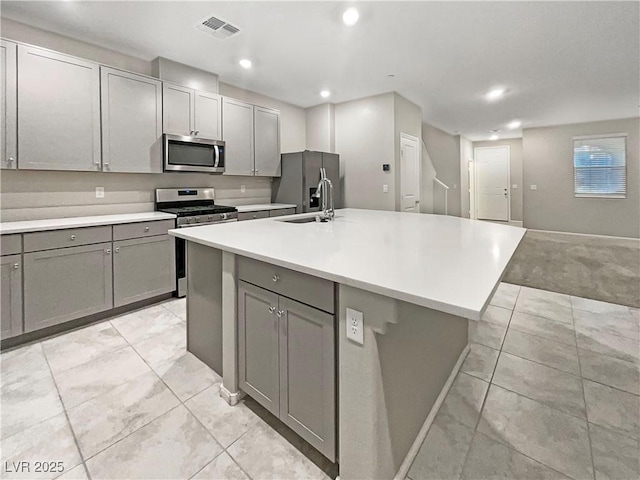 kitchen with gray cabinetry, stainless steel appliances, sink, and a center island with sink