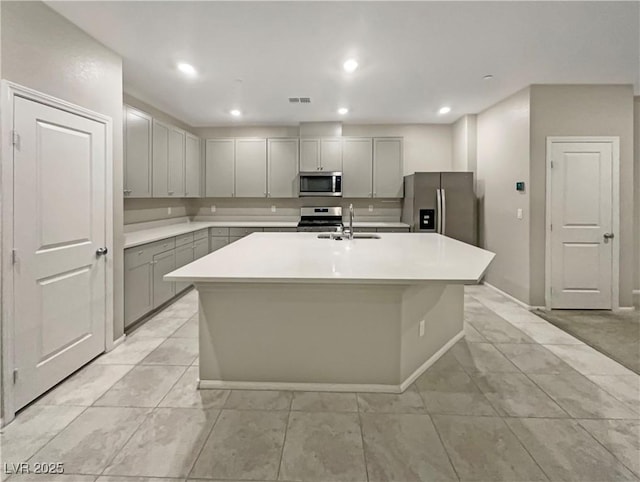 kitchen with stainless steel appliances, gray cabinetry, an island with sink, and sink