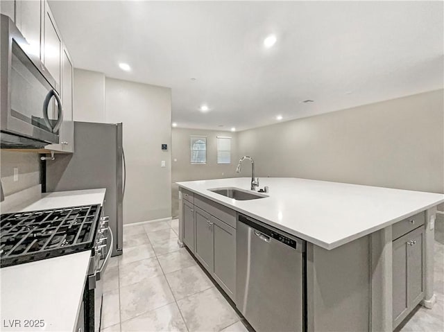 kitchen with stainless steel appliances, a kitchen island with sink, gray cabinets, and sink