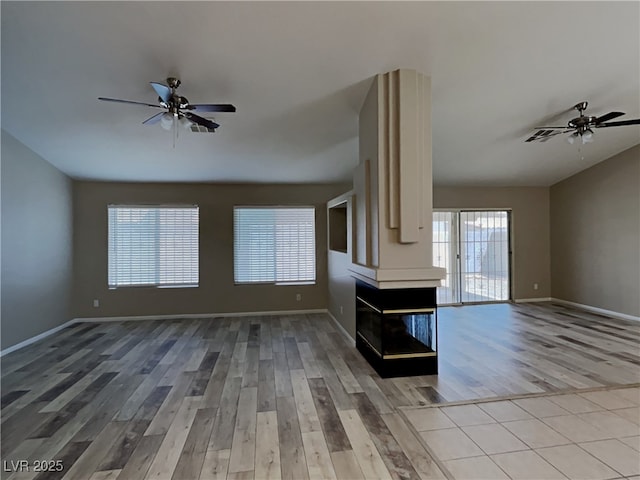 unfurnished living room featuring a multi sided fireplace, light wood-type flooring, and ceiling fan