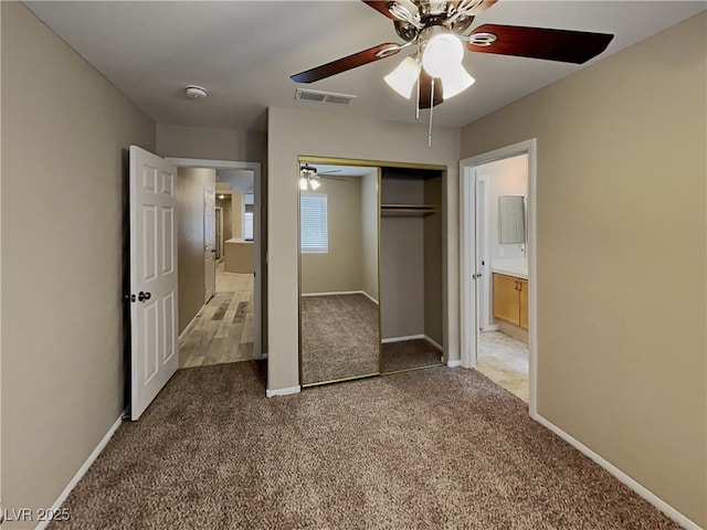 unfurnished bedroom featuring a closet, ensuite bath, carpet floors, and ceiling fan