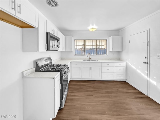 kitchen featuring stainless steel appliances, ornamental molding, dark wood-type flooring, sink, and white cabinetry