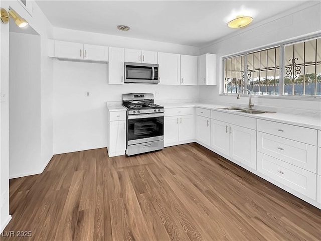 kitchen with appliances with stainless steel finishes, white cabinets, hardwood / wood-style floors, and sink