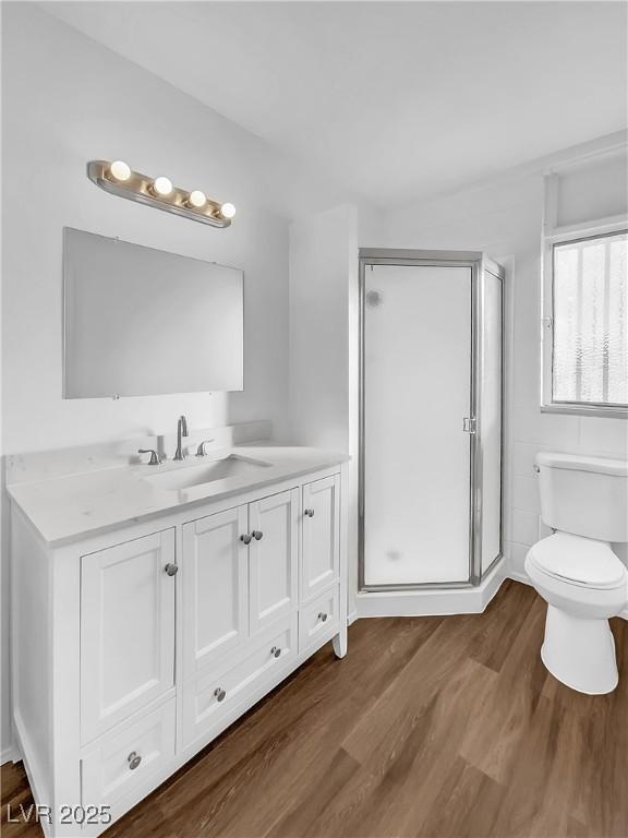 bathroom featuring toilet, wood-type flooring, vanity, and a shower with door