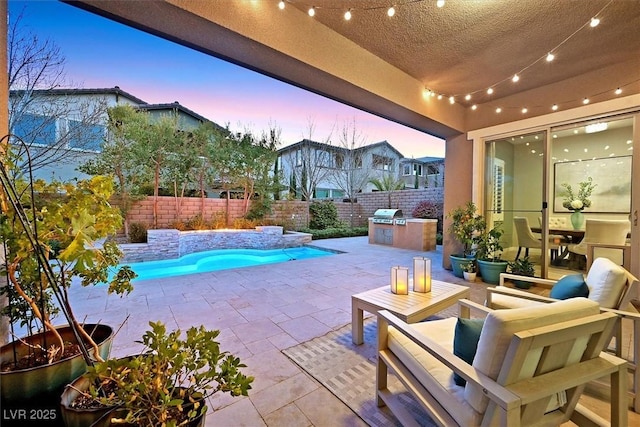 pool at dusk with an outdoor kitchen and a patio