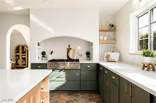 kitchen with stainless steel gas stovetop, light stone counters, green cabinetry, and tasteful backsplash