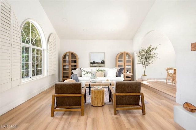 living room featuring high vaulted ceiling, arched walkways, light wood-type flooring, and baseboards