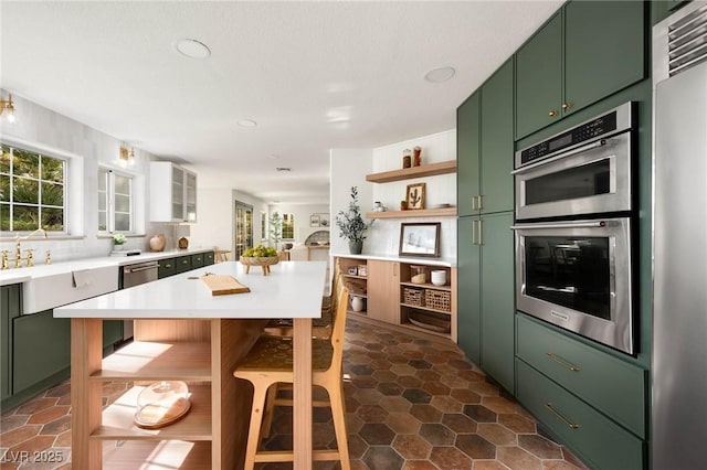 kitchen with green cabinetry, open shelves, stainless steel appliances, light countertops, and backsplash