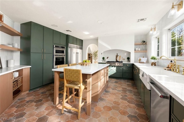 kitchen featuring visible vents, open shelves, green cabinets, appliances with stainless steel finishes, and a sink