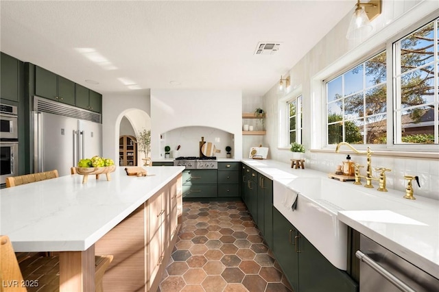 kitchen with visible vents, dark tile patterned floors, backsplash, stainless steel appliances, and green cabinets