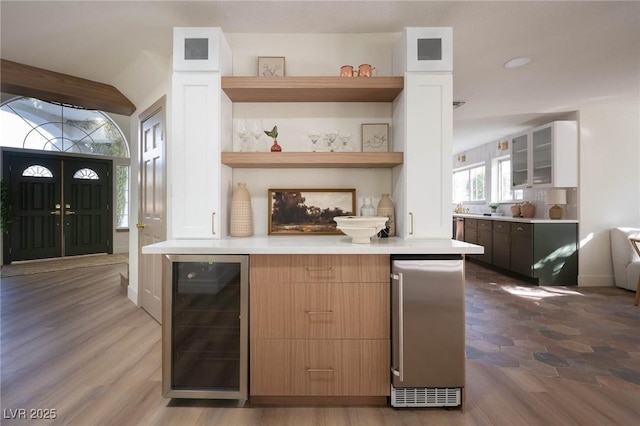 kitchen featuring open shelves, fridge, wine cooler, light countertops, and glass insert cabinets