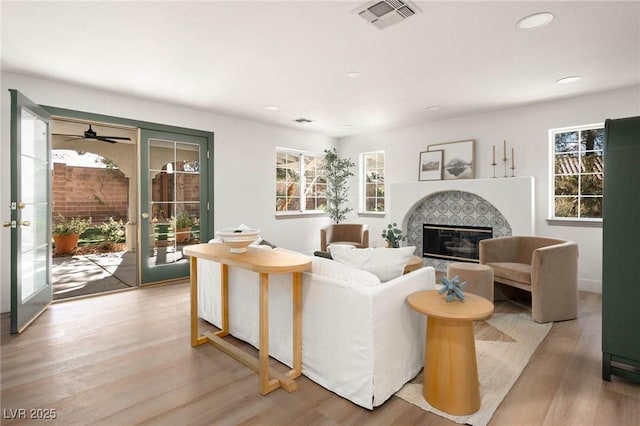 living area with visible vents, light wood finished floors, recessed lighting, french doors, and a glass covered fireplace