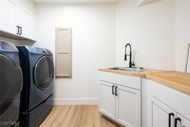 laundry area featuring baseboards, cabinet space, a sink, light wood-style floors, and washing machine and dryer