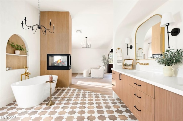 bathroom featuring vanity, visible vents, an inviting chandelier, a multi sided fireplace, and a freestanding bath