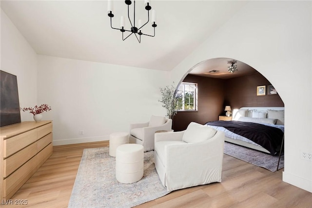 bedroom with arched walkways, light wood-type flooring, baseboards, and vaulted ceiling