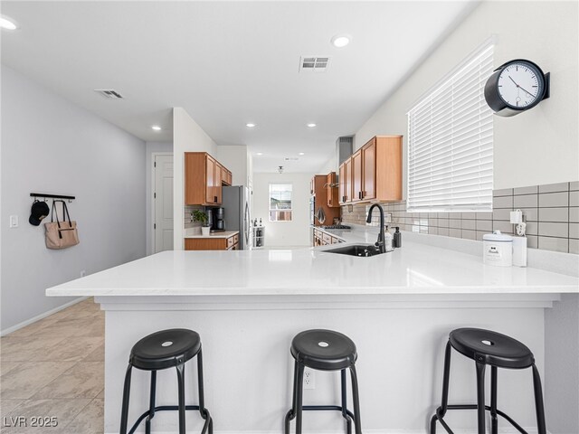 kitchen featuring sink, tasteful backsplash, a kitchen bar, and kitchen peninsula