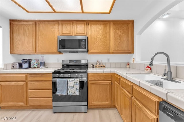 kitchen featuring tile counters, appliances with stainless steel finishes, sink, and light hardwood / wood-style floors