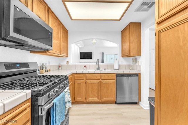 kitchen featuring appliances with stainless steel finishes, sink, tile countertops, and light hardwood / wood-style floors