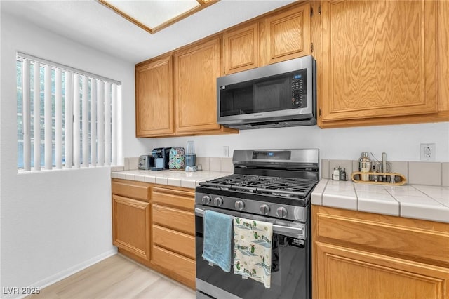 kitchen featuring light wood-type flooring, stainless steel appliances, and tile countertops