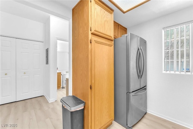 kitchen with light brown cabinets, electric panel, light hardwood / wood-style flooring, and stainless steel fridge