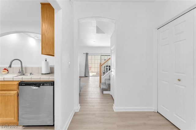 kitchen featuring sink, stainless steel dishwasher, light hardwood / wood-style flooring, and tile counters