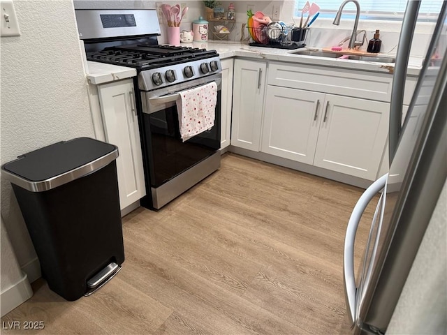 kitchen featuring sink, stainless steel appliances, white cabinetry, and light hardwood / wood-style floors