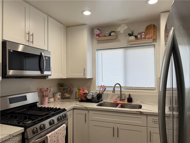 kitchen with appliances with stainless steel finishes, white cabinets, light stone counters, and sink