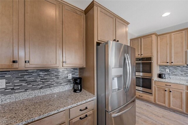 kitchen featuring light stone countertops, decorative backsplash, light wood-type flooring, and appliances with stainless steel finishes