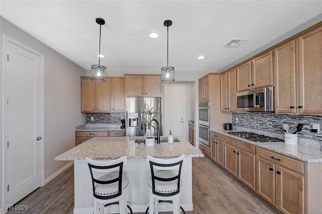 kitchen featuring sink, light hardwood / wood-style floors, hanging light fixtures, a kitchen island with sink, and appliances with stainless steel finishes