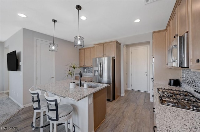 kitchen with light stone counters, light hardwood / wood-style flooring, stainless steel appliances, backsplash, and sink