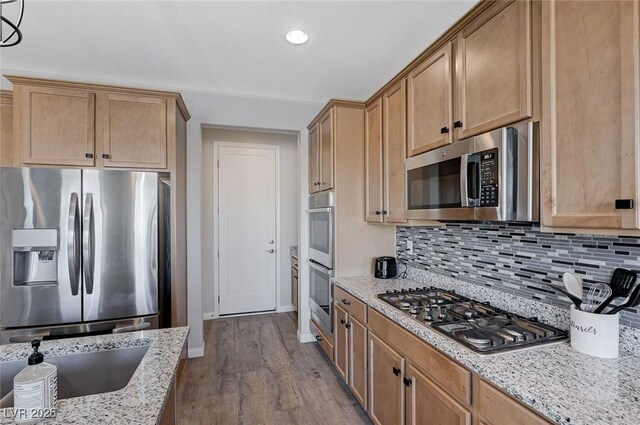 kitchen with light stone counters, hardwood / wood-style flooring, appliances with stainless steel finishes, and decorative backsplash