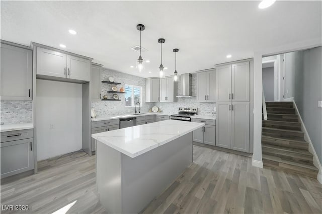 kitchen with stainless steel appliances, a center island, pendant lighting, sink, and wall chimney range hood