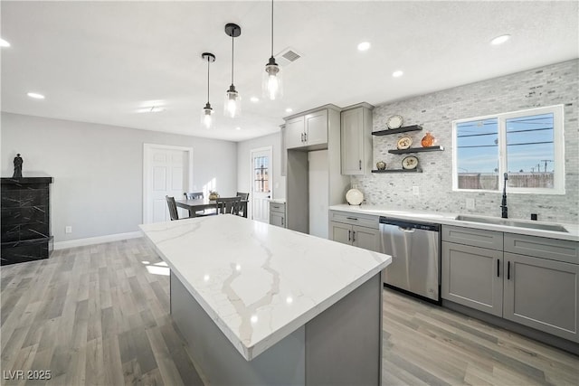 kitchen with decorative light fixtures, a center island, dishwasher, light stone counters, and gray cabinetry