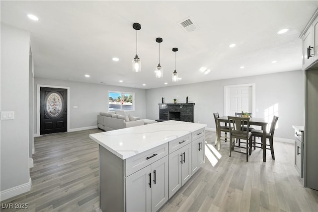 kitchen featuring a center island, light wood-type flooring, hanging light fixtures, and light stone countertops