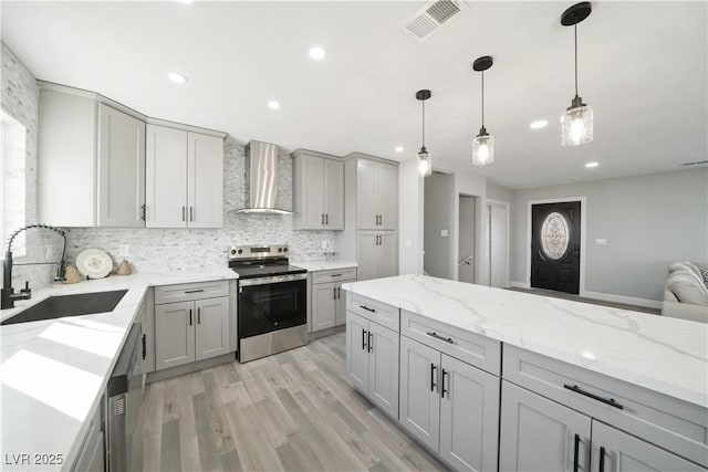 kitchen featuring appliances with stainless steel finishes, gray cabinetry, light wood-type flooring, sink, and wall chimney range hood