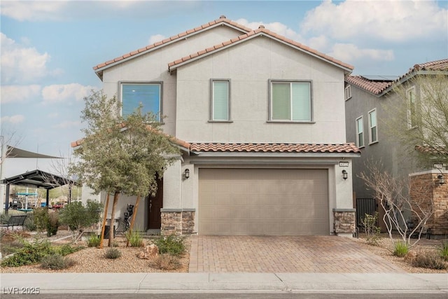 mediterranean / spanish-style home featuring decorative driveway, a tile roof, stucco siding, an attached garage, and stone siding