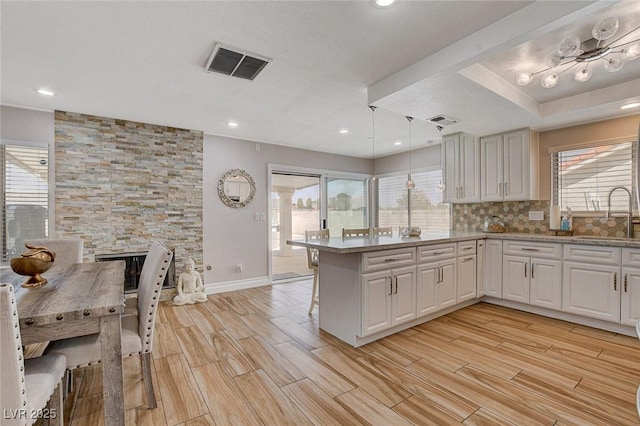 kitchen featuring kitchen peninsula, pendant lighting, white cabinetry, a fireplace, and sink