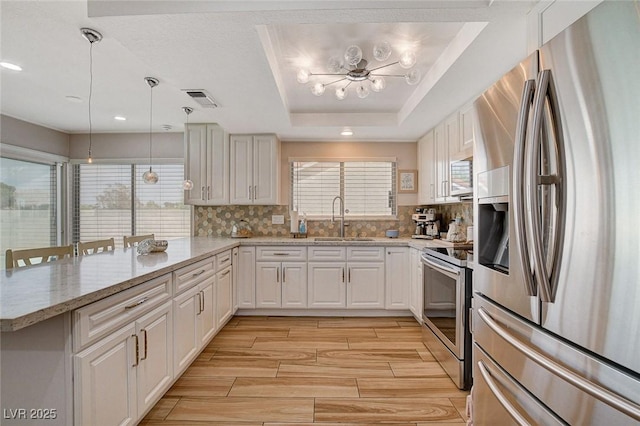 kitchen featuring kitchen peninsula, a raised ceiling, a kitchen bar, appliances with stainless steel finishes, and sink