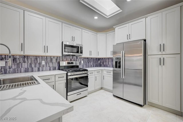 kitchen with stainless steel appliances, sink, white cabinetry, light stone counters, and tasteful backsplash