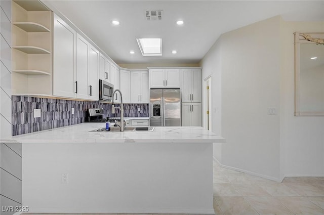 kitchen with appliances with stainless steel finishes, light stone countertops, kitchen peninsula, white cabinets, and backsplash