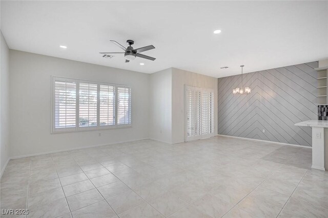 unfurnished living room featuring wood walls, ceiling fan with notable chandelier, and light tile patterned floors