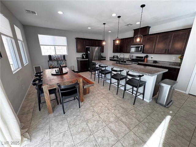 kitchen featuring stainless steel appliances, sink, decorative light fixtures, a kitchen bar, and an island with sink