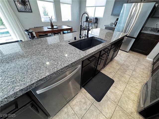 kitchen with stainless steel appliances, light tile patterned flooring, light stone countertops, and sink