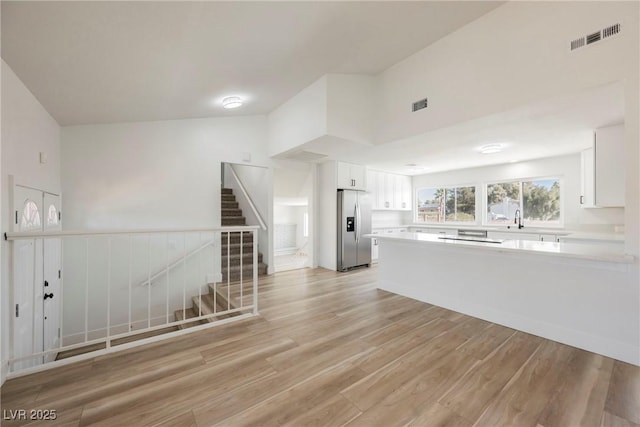 kitchen featuring light wood-type flooring, kitchen peninsula, stainless steel fridge, white cabinets, and sink