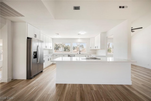 kitchen with sink, white cabinets, light hardwood / wood-style floors, stainless steel refrigerator with ice dispenser, and black electric stovetop