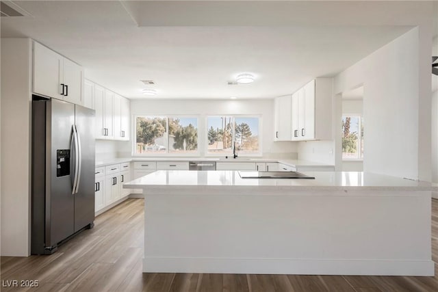 kitchen featuring stainless steel appliances, light wood-type flooring, light stone counters, sink, and white cabinetry