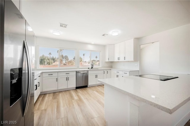 kitchen with appliances with stainless steel finishes, kitchen peninsula, light stone countertops, white cabinets, and sink