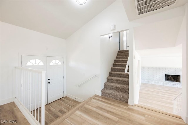 foyer entrance featuring high vaulted ceiling, a fireplace, and hardwood / wood-style flooring