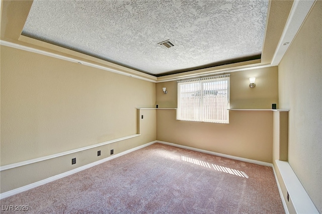 empty room with a tray ceiling, carpet, visible vents, a textured ceiling, and baseboards